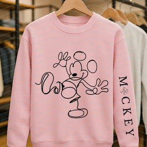 Puede incluir: Una sudadera de cuello redondo en color rosa claro con un dibujo de l&iacute;nea continua negra de Mickey Mouse en la parte frontal. La manga izquierda muestra el texto "MICKEY" impreso verticalmente en una fuente serif negra, con un peque&ntilde;o icono gr&aacute;fico sobre la M.
