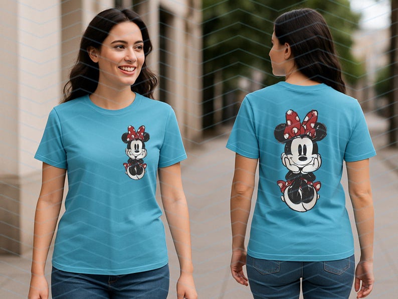 May include: A light blue t-shirt featuring a Minnie Mouse graphic on the front and back. The graphic shows Minnie Mouse wearing a red bow with white polka dots. The t-shirt is short-sleeved and made of a soft material.