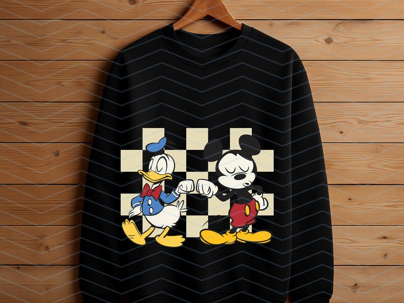 May include: Black sweatshirt featuring a graphic of Donald Duck and Mickey Mouse bumping fists. The characters are set against a checkered background. Donald Duck is wearing a blue sailor suit and Mickey Mouse is wearing red shorts.