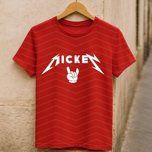 May include: Red t-shirt with the word "MICKE" in a stylized, white font, and a white hand gesture. The shirt is hanging on a wooden hanger against a neutral background. The shirt has a chevron pattern.
