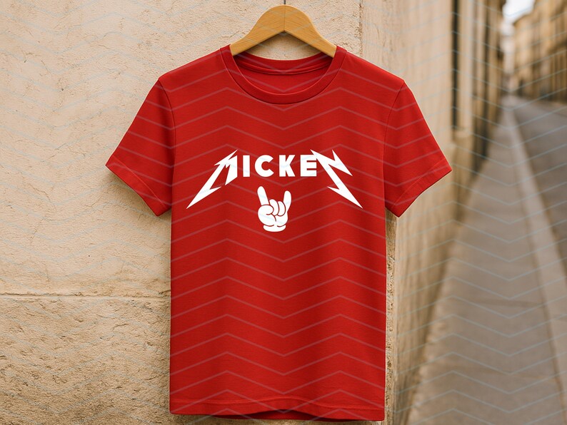 May include: Red t-shirt with the word "MICKE" in a stylized, white font, and a white hand gesture. The shirt is hanging on a wooden hanger against a neutral background. The shirt has a chevron pattern.