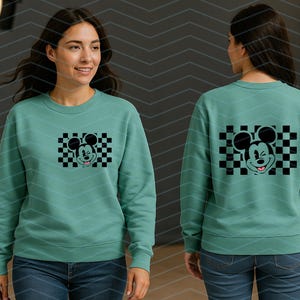 May include: A teal green sweatshirt with a black and white checkered graphic of Mickey Mouse winking. The graphic is centered on the front of the sweatshirt.