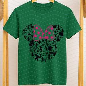 May include: A dark green short-sleeve t-shirt featuring a subtle horizontal chevron pattern. The center displays a large black silhouette of a mouse head shape filled with various small character figures and stars, topped with a bright pink polka-dot bow.