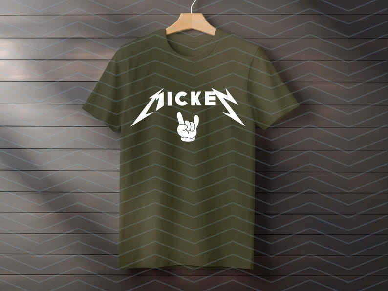 May include: Olive green t-shirt with the word "MICKE" in a stylized white font, with a hand gesture below. The design is reminiscent of a rock band logo. The shirt is hanging on a wooden hanger.