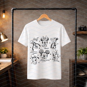 May include: White t-shirt featuring black and white illustrations of Disney characters, including Mickey Mouse, Minnie Mouse, and Donald Duck. The shirt has a crew neck and short sleeves. The names of the characters are written below each illustration.
