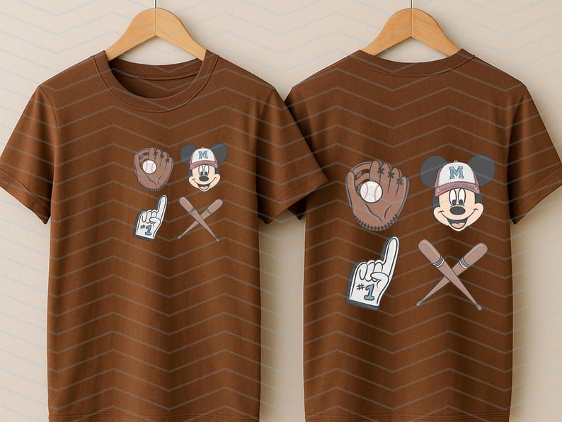 May include: Two brown t-shirts with a baseball theme featuring Mickey Mouse. One shirt has Mickey Mouse holding a baseball glove and the other has Mickey Mouse holding a baseball bat and a number one finger.