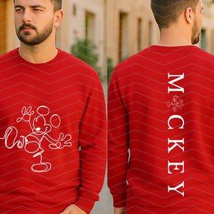 Puede incluir: Una sudadera roja de manga larga con un gr&aacute;fico de l&iacute;neas blancas de un rat&oacute;n de dibujos animados en la parte delantera. La parte posterior muestra el texto vertical blanco "MCKEY" con un peque&ntilde;o gr&aacute;fico de rat&oacute;n a juego sobre las letras.