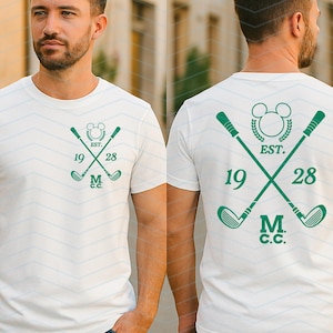 May include: White t-shirt with a green golf-themed design. The design features crossed golf clubs, a Mickey Mouse silhouette, the text "EST. 1928", and "M.C.C.". The same design is on the front and back of the shirt.