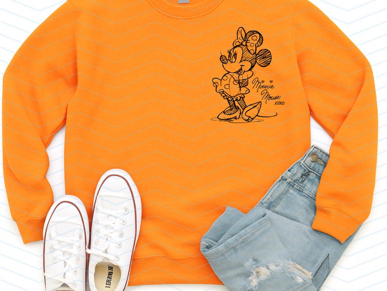 May include: An orange sweatshirt featuring a sketch of Minnie Mouse with the text "Minnie Mouse xoxo". The image also includes white sneakers and blue jeans.
