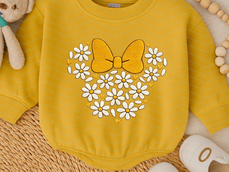 Puede incluir: Body de beb&eacute; amarillo mostaza con dise&ntilde;o de lazo y margaritas. El dise&ntilde;o presenta un lazo amarillo y margaritas blancas con centros amarillos dispuestas en forma de cabeza de Mickey Mouse. El body tiene mangas largas.