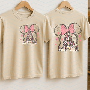 Pu&ograve; includere: Due magliette beige con una stampa grafica di un fiocco rosa e un castello. Il castello &egrave; circondato da cuori e stelle rosa.