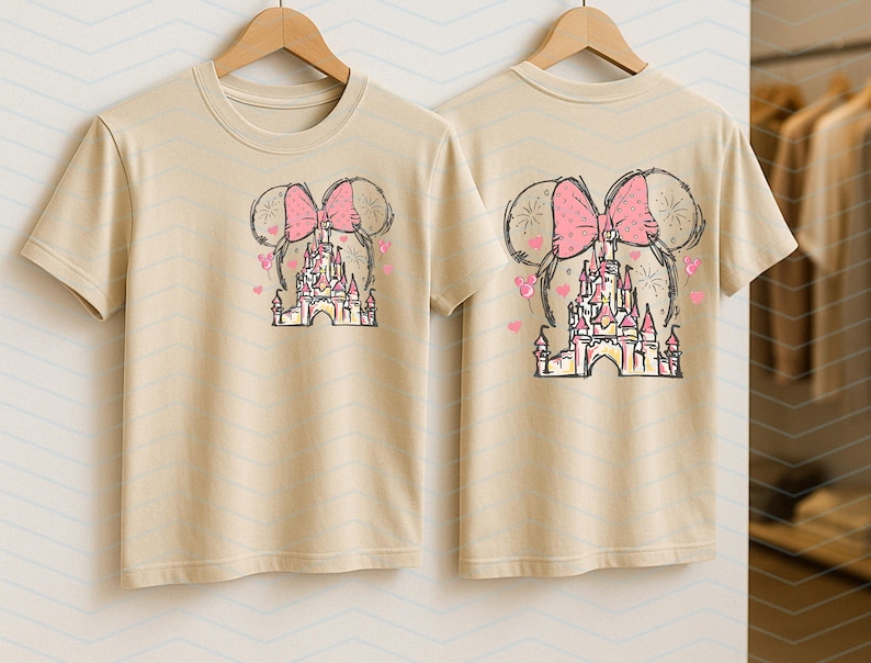 Pu&ograve; includere: Due magliette beige con una stampa grafica di un fiocco rosa e un castello. Il castello &egrave; circondato da cuori e stelle rosa.