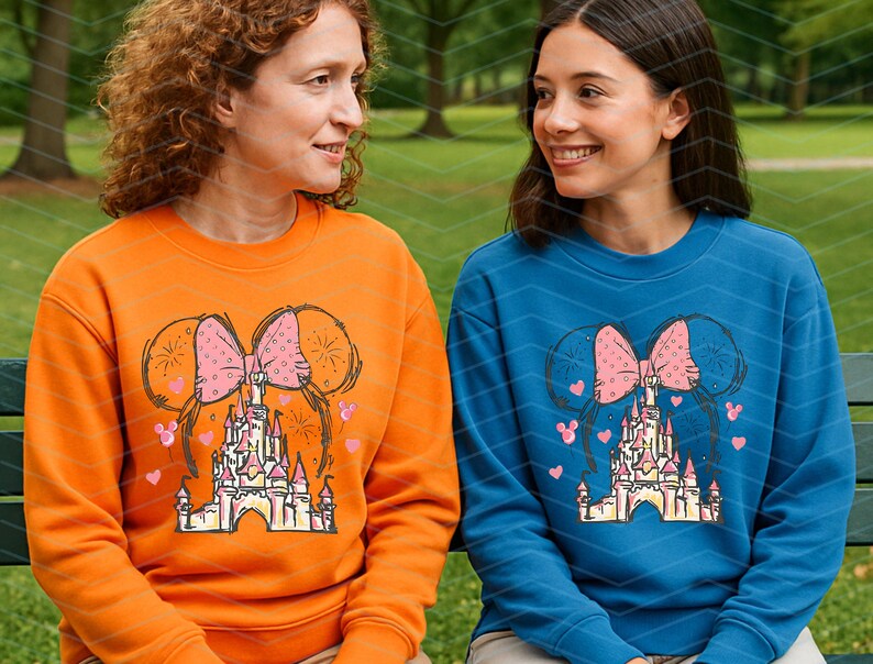 Pu&ograve; includere: Due persone indossano felpe arancioni e blu con un fiocco rosa e una grafica di un castello. La grafica presenta un fiocco rosa con un castello al centro e cuori rosa e fuochi d'artificio intorno.