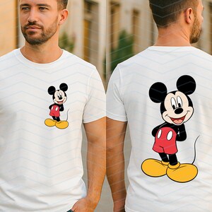 May include: A white short-sleeved t-shirt featuring a small graphic of Mickey Mouse on the left chest and a large matching graphic of Mickey Mouse on the back. The character is depicted with black ears, a red pair of shorts, and yellow shoes.
