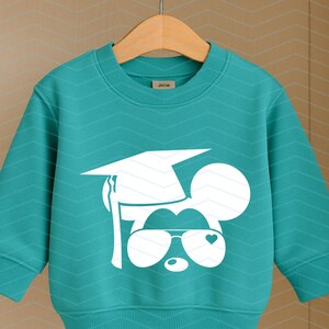 May include: Teal sweatshirt featuring a white graphic of a mouse wearing a graduation cap and sunglasses with a heart detail. The sweatshirt has a crew neck and long sleeves. The design is centered on the front of the garment.