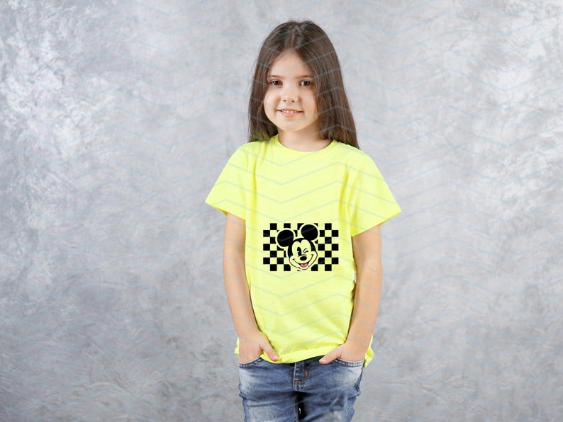 May include: A young person wearing a bright yellow t-shirt with a black and white checkered design featuring Mickey Mouse's face.
