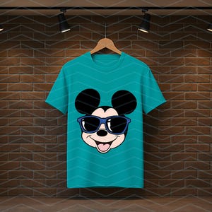 K&ouml;nnte beinhalten: Ein kurz&auml;rmeliges T-Shirt in Petrol mit einem Grafikdruck von Mickey Mouse, der eine dunkelblaue Sonnenbrille tr&auml;gt. Das Charakterdesign zeigt die ikonischen runden Ohren, ein l&auml;chelndes Gesicht mit offenem Mund und eine schwarze Nase.