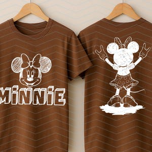 May include: Brown t-shirt with a white Minnie Mouse design on the front and back. The front displays Minnie's face and the name "Minnie". The back shows a full-body illustration of Minnie Mouse. The t-shirt is displayed on a wooden hanger.