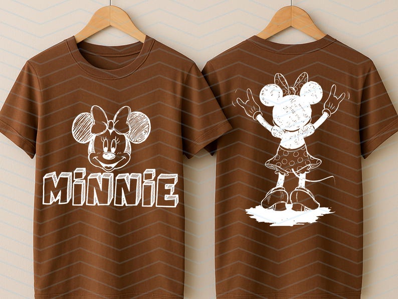 May include: Brown t-shirt with a white Minnie Mouse design on the front and back. The front displays Minnie's face and the name "Minnie". The back shows a full-body illustration of Minnie Mouse. The t-shirt is displayed on a wooden hanger.
