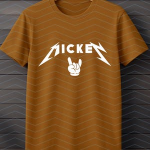 May include: Mustard-colored t-shirt with a white graphic. The graphic features the word "MICKEY" in a stylized font with lightning bolt accents and a hand making a rock and roll gesture.