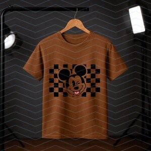 May include: A brown t-shirt with a black and white checkered pattern and a black Mickey Mouse graphic with a pink tongue sticking out.