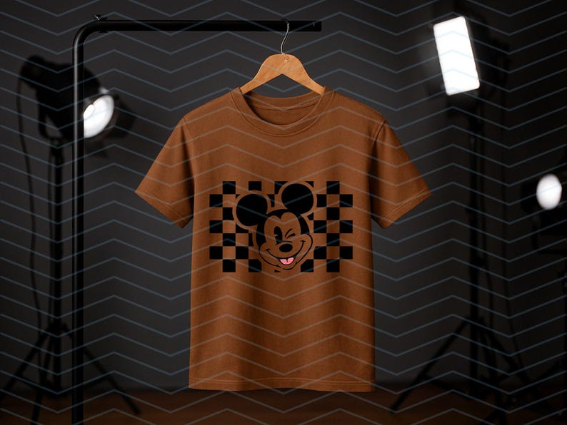 May include: A brown t-shirt with a black and white checkered pattern and a black Mickey Mouse graphic with a pink tongue sticking out.