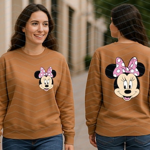 May include: A brown sweatshirt featuring a Minnie Mouse graphic on the front and back. The Minnie Mouse design includes a pink bow with white polka dots. The sweatshirt is a long-sleeved, crew neck style.