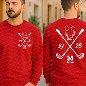 May include: A red sweatshirt with a white golf-themed design. The design includes crossed golf clubs, the text "EST. 1928", and the initials "M.C.C." The sweatshirt is a solid red color.