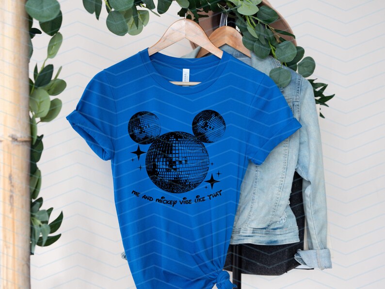 Puede incluir: Una camiseta azul real con un gr&aacute;fico negro de la cabeza de Mickey Mouse hecha de bolas de discoteca. El texto "Me and Mickey vibe like that" est&aacute; impreso debajo del gr&aacute;fico.