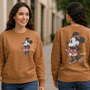 K&ouml;nnte beinhalten: Ein braunes Sweatshirt mit einem Minnie Mouse-Motiv auf der Vorder- und R&uuml;ckseite. Das Motiv zeigt Minnie Mouse in einem roten gepunkteten Kleid und braunen Schuhen. Das Wort "Disney" ist darunter gedruckt.