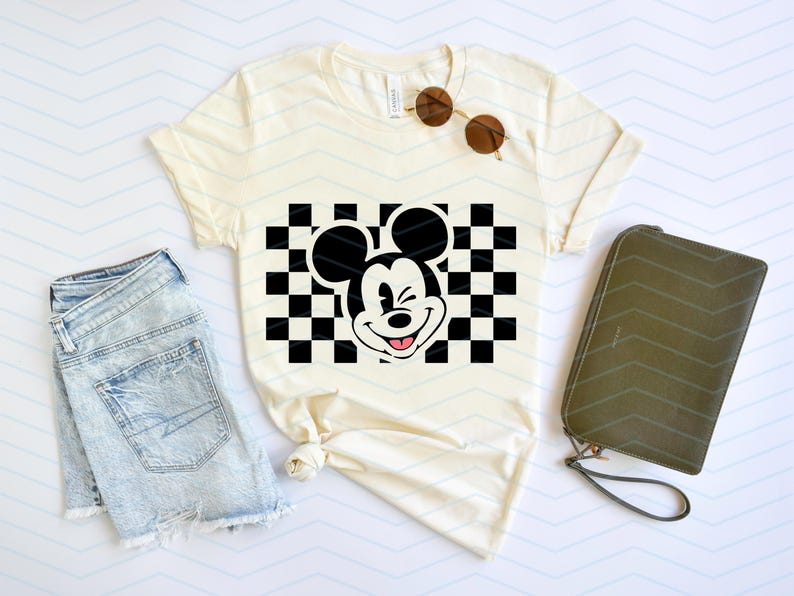 May include: A white t-shirt with a black and white checkered pattern and a black and white cartoon image of Mickey Mouse winking. The Mickey Mouse image is in the center of the checkered pattern.