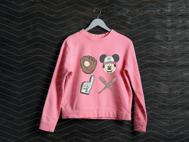 May include: Pink sweatshirt with a Mickey Mouse baseball graphic. The graphic includes a baseball glove, a baseball bat, and a number one finger. The Mickey Mouse character is wearing a baseball cap with the letter "M" on it.