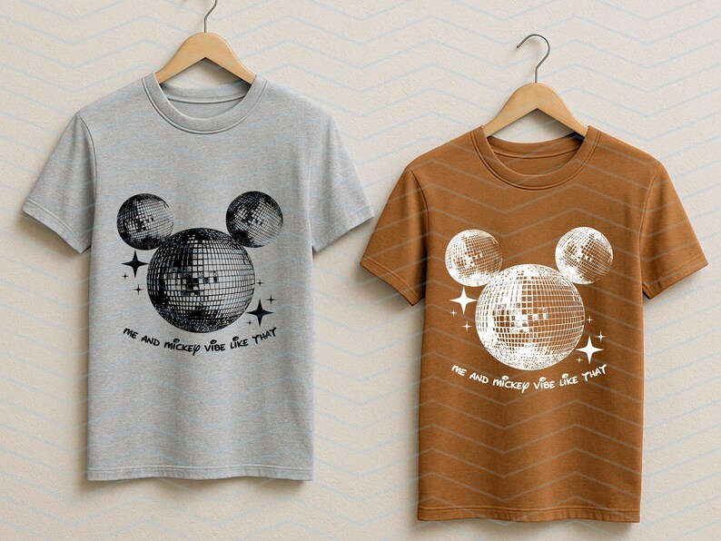 Puede incluir: Dos camisetas con un gr&aacute;fico de la cabeza de Mickey Mouse hecha de bolas de discoteca. El texto en las camisetas dice "Me and Mickey vibe like that". Una camiseta es gris y la otra es marr&oacute;n.