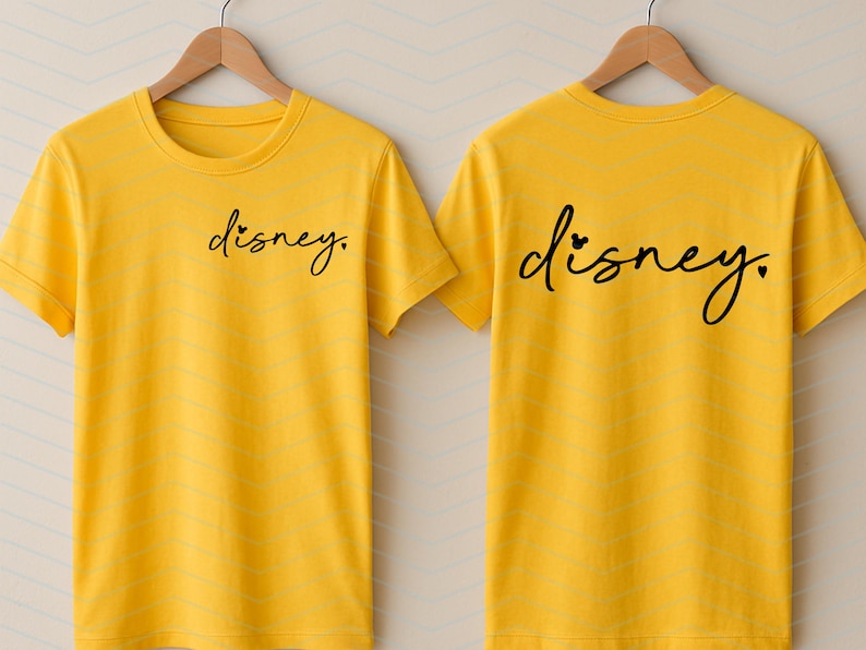 Op de afbeelding: Twee gele t-shirts met het woord "disney" in zwart script. E&eacute;n shirt heeft de tekst op de voorkant, de andere op de achterkant. Het woord "disney" heeft een hartje boven de "i".