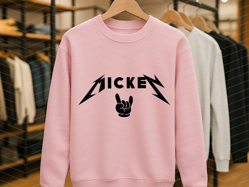 May include: A light pink crew neck sweatshirt with the word "MICKE" in a black, stylized font, with a rock and roll hand gesture graphic. Other sweatshirts are visible in the background.