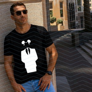 May include: A black short-sleeved t-shirt featuring a white graphic print of a stylized suit jacket, a necktie, and a pair of circular ears positioned above the collar. The design is centered on the chest of the garment.