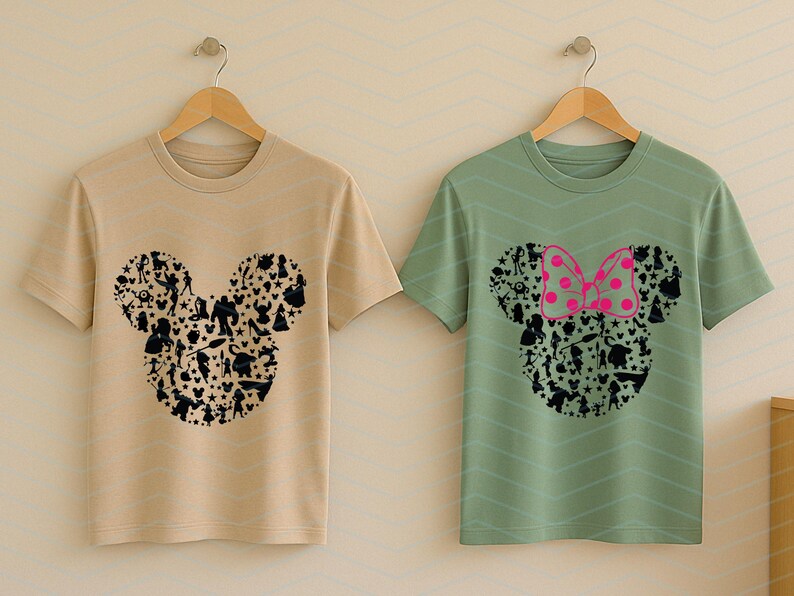 May include: Two short-sleeve crew neck t-shirts hanging on wooden hangers. The left shirt is beige with a black graphic of a Mickey Mouse head silhouette filled with various character shapes. The right shirt is sage green with a similar black silhouette graphic featuring a bright pink polka-dot bow.