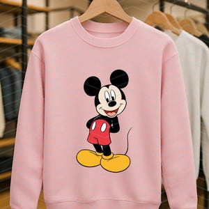 May include: A light pink crewneck sweatshirt featuring a centered graphic of Mickey Mouse. The character is depicted with his signature black ears, red shorts with two white buttons, and large yellow shoes, standing in a classic pose on the front.