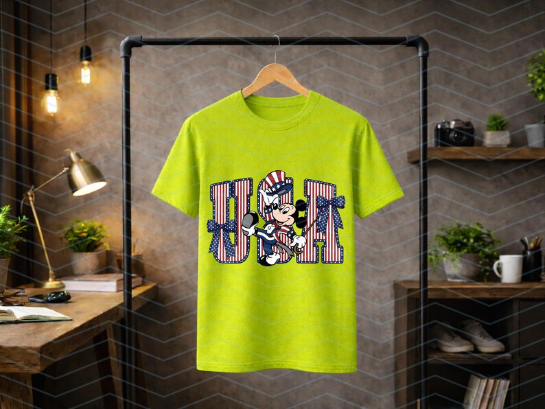 May include: A lime green short-sleeve t-shirt featuring a graphic of Mickey Mouse wearing a patriotic hat. The letters USA are printed in a red and white striped pattern with blue stars, accented by two blue patterned bows on the sides.