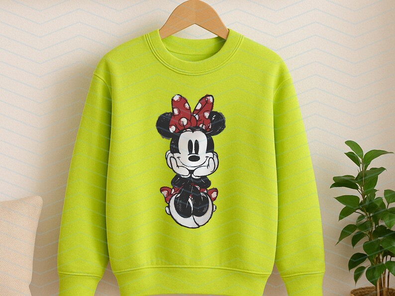 May include: A lime green sweatshirt featuring a graphic of Minnie Mouse. Minnie Mouse is depicted in black and white with a red polka dot bow and matching accents. The sweatshirt has a crew neck and long sleeves, suitable for children.