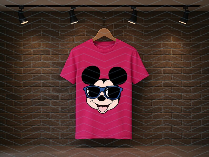 K&ouml;nnte beinhalten: Ein leuchtend pinkfarbenes Kurzarm-T-Shirt mit einem Grafikdruck von Mickey Mouse, der eine blau umrandete Sonnenbrille tr&auml;gt. Die Figur hat gro&szlig;e schwarze Ohren, ein l&auml;chelndes Gesicht und ist mittig auf der Vorderseite platziert.