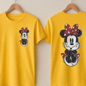 May include: Two yellow t-shirts with a Minnie Mouse graphic. One shirt has a small graphic on the front, the other has a large graphic on the back. The Minnie Mouse design features a red bow with white polka dots.