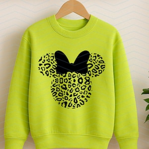 May include: A neon green sweatshirt featuring a black bow and a leopard print design in the shape of a mouse head. The sweatshirt is hanging on a wooden hanger.