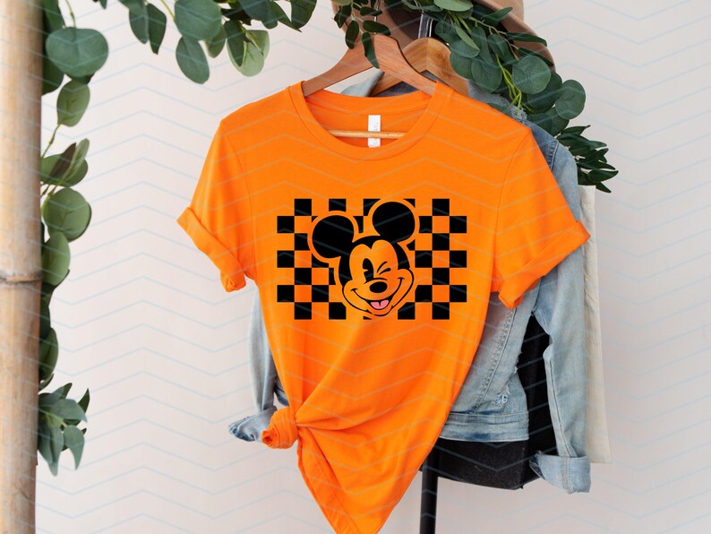 May include: Orange t-shirt with a black and white checkered pattern and a cartoon image of Mickey Mouse with a mischievous grin.