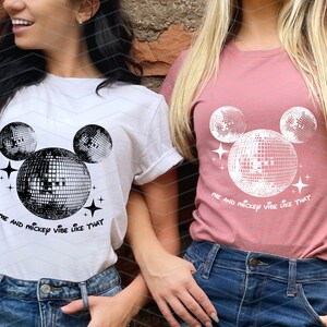 Puede incluir: Dos camisetas blancas con un gr&aacute;fico en blanco y negro de la cabeza de Mickey Mouse hecha de bolas de discoteca. El texto en las camisetas dice "Me and Mickey vibe like that".
