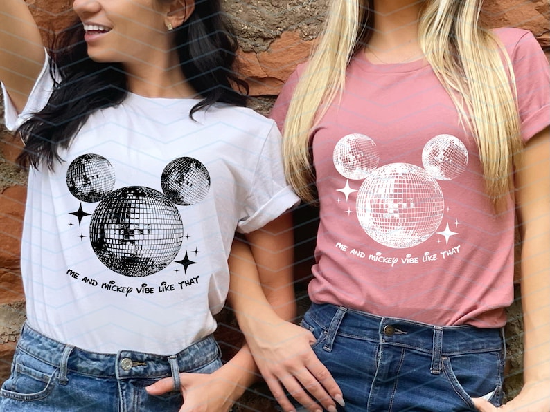 Puede incluir: Dos camisetas blancas con un gr&aacute;fico en blanco y negro de la cabeza de Mickey Mouse hecha de bolas de discoteca. El texto en las camisetas dice "Me and Mickey vibe like that".