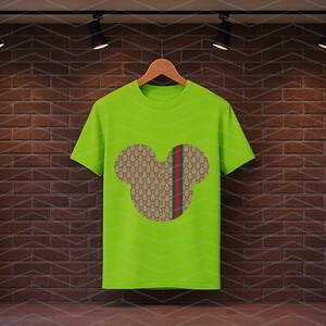 Puede incluir: Una camiseta de manga corta de color verde lima brillante con un gr&aacute;fico central de una silueta de cabeza de rat&oacute;n. La silueta est&aacute; rellena con un patr&oacute;n repetitivo en tonos tostado y marr&oacute;n e incluye una franja vertical roja y verde.