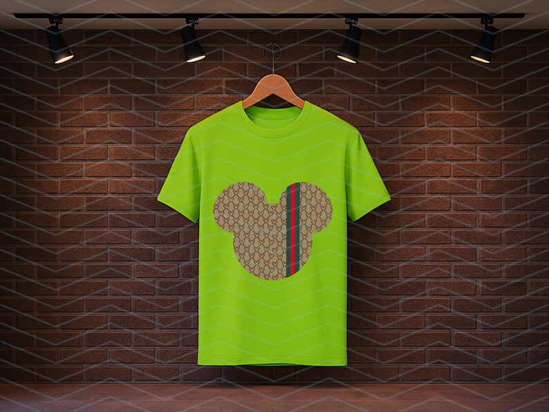 Puede incluir: Una camiseta de manga corta de color verde lima brillante con un gr&aacute;fico central de una silueta de cabeza de rat&oacute;n. La silueta est&aacute; rellena con un patr&oacute;n repetitivo en tonos tostado y marr&oacute;n e incluye una franja vertical roja y verde.
