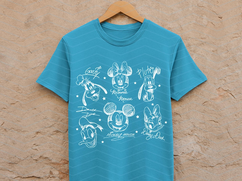 May include: A turquoise t-shirt featuring a white sketch design of Disney characters, including Mickey Mouse, Minnie Mouse, Donald Duck, Daisy Duck, Goofy, and Pluto. The shirt has a crew neck and short sleeves.