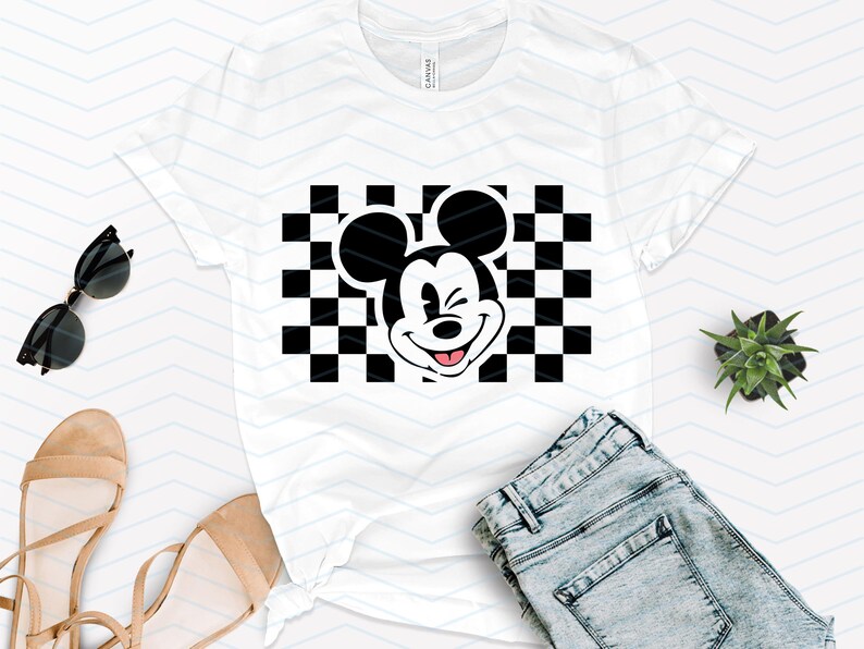 May include: White t-shirt with a black and white checkered pattern and a black and white image of Mickey Mouse winking. Mickey Mouse is wearing a red tongue.
